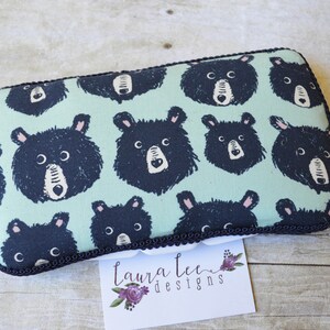 May include: Rectangular pouch with a repeating pattern of black bear faces on a light teal background. The pouch has a black trim and a white tag with the text "Laura Lee Designs".