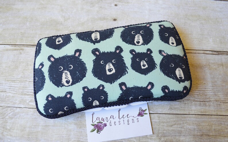 May include: Rectangular pouch with a repeating pattern of black bear faces on a light teal background. The pouch has a black trim and a white tag with the text "Laura Lee Designs".