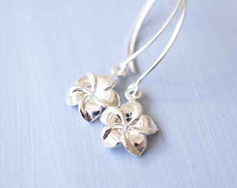 May include: Silver dangle earrings featuring a detailed plumeria flower design.