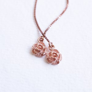 Könnte beinhalten: Ohrringe mit Rosenanhängern aus Roségold. Die Ohrringe haben eine feine Kette, die durch das Ohr gefädelt wird, mit den Rosenanhängern, die darunter hängen. Ein schönes Accessoire für den Alltag.
