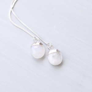 May include: A silver chain necklace with two moonstone pendants. The moonstones are a milky white colour and have a silver trim.