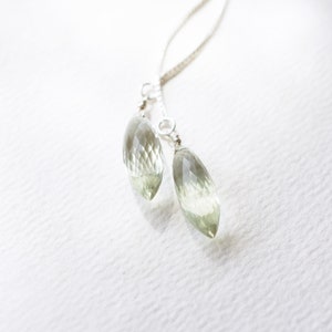 Puede incluir: Un collar de cadena de plata con dos colgantes de piedra preciosa verde claro en forma de lágrima.