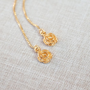 Könnte beinhalten: Ein Paar goldene Kettenohrringe mit einem rosenförmigen Anhänger am Ende jeder Kette.