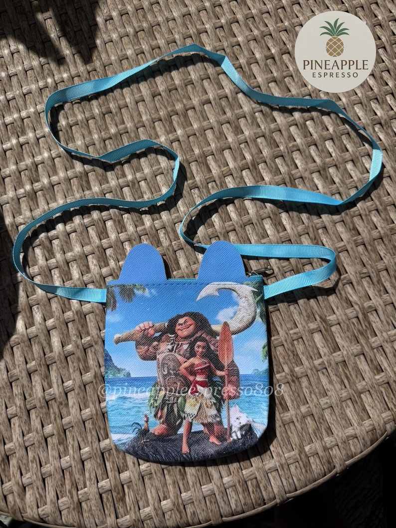 Puede incluir: Una peque&ntilde;a bolsa azul con una correa azul claro, con un gr&aacute;fico colorido de personajes de una popular pel&iacute;cula de animaci&oacute;n. La bolsa tiene dos acentos azules en forma de oreja en la parte superior. El texto "@pineapplepress808" es visible.
