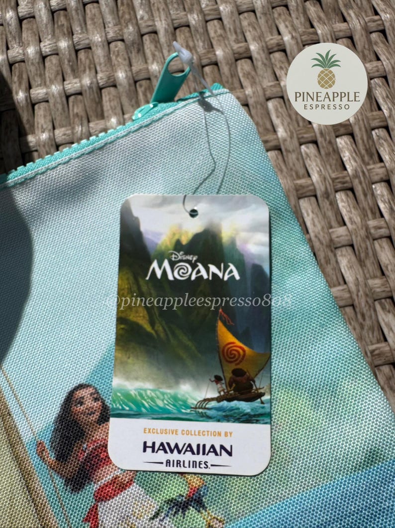Puede incluir: Una bolsa con cremallera azul claro con un dise&ntilde;o de Disney Moana. La bolsa tiene una etiqueta que dice "Moana" y "Exclusive Collection by Hawaiian Airlines". La bolsa tiene una cremallera turquesa y una leng&uuml;eta a juego.