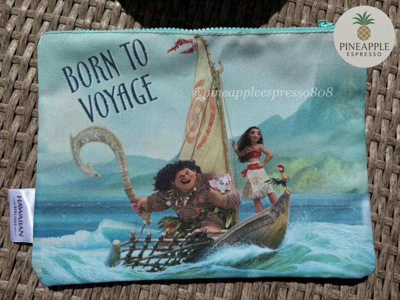 Puede incluir: Una bolsa con cremallera con una colorida ilustraci&oacute;n de personajes en un barco navegando por el oc&eacute;ano. El texto "BORN TO VOYAGE" est&aacute; impreso en la parte superior izquierda. La bolsa tiene una cremallera turquesa y una etiqueta de Hawaiian Airlines.
