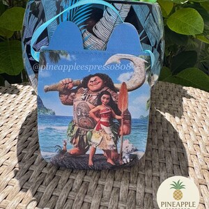Puede incluir: Un recipiente con estampado azul y blanco con un asa azul y una peque&ntilde;a bolsa con personajes de la pel&iacute;cula Moana. La bolsa tiene un asa azul y el texto "@pineappleespresso808". Un logotipo de pi&ntilde;a es visible.