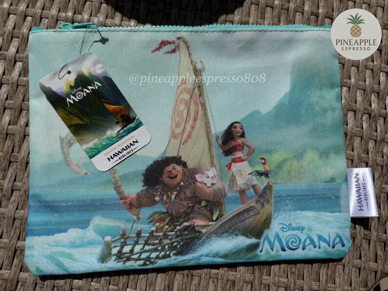 Puede incluir: Una bolsa con cremallera azul claro con un dise&ntilde;o de Disney Moana. La bolsa muestra personajes de la pel&iacute;cula en un barco, con una etiqueta que dice "Moana" y "Hawaiian Airlines". La bolsa tiene una cremallera turquesa y una peque&ntilde;a etiqueta blanca.