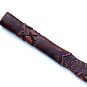 May include: A dark brown, carved wooden staff or handle. The wood has a rich, warm tone with intricate leaf and diamond patterns carved along its length. The end is a solid, unadorned cylinder.