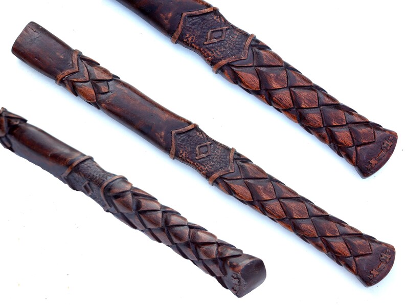 May include: Three dark brown, carved wooden handles with intricate woven and geometric patterns. The handles are displayed at different angles, showcasing the detailed craftsmanship and texture of the wood.