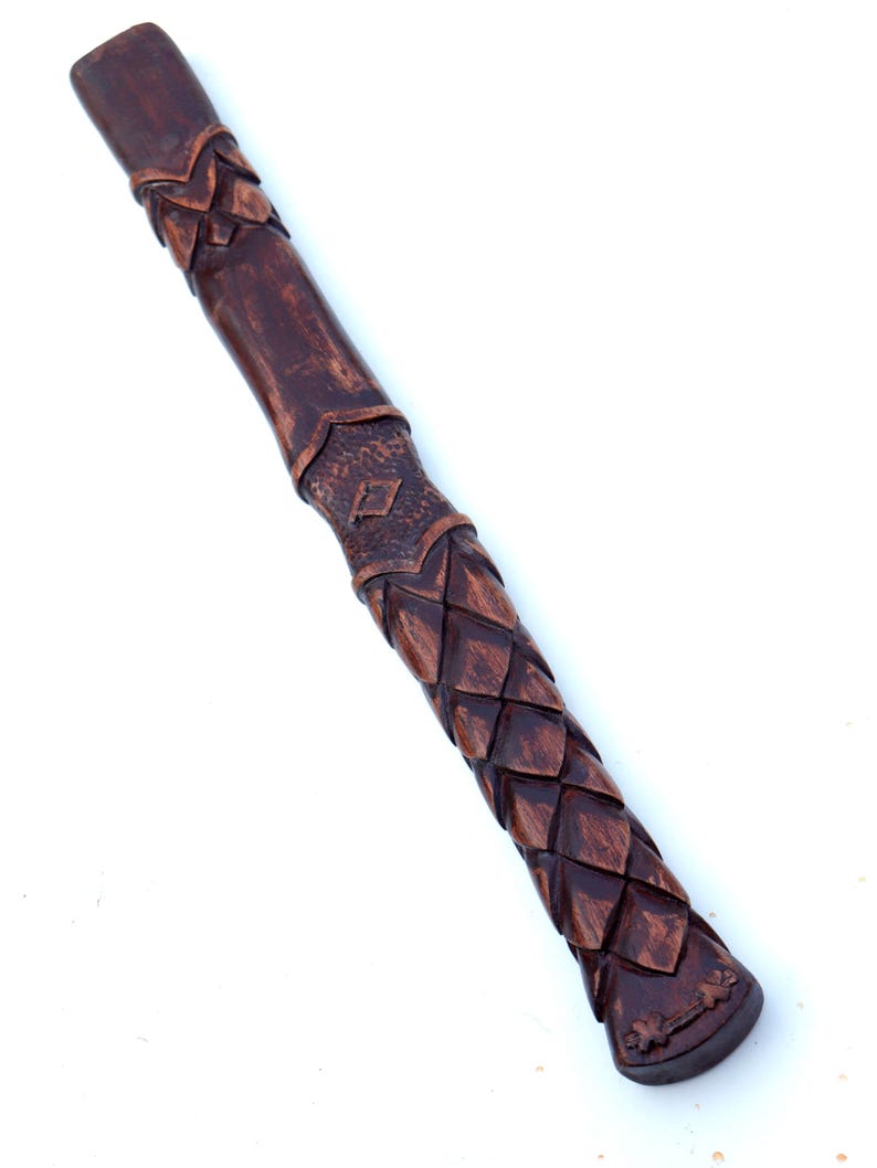 May include: A brown, carved wooden handle with a textured, scale-like pattern. The handle has a dark finish and is angled diagonally against a white background. The design includes diamond and leaf-like details.