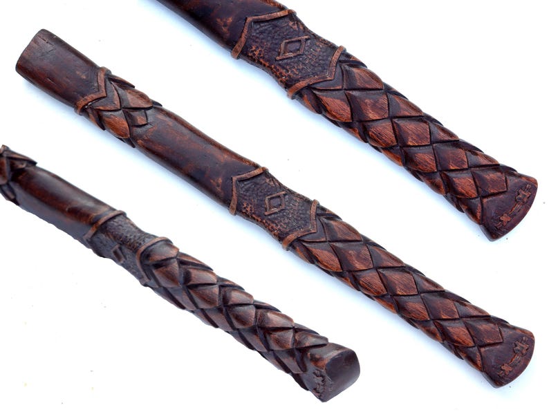 May include: Three dark brown, carved wooden handles with intricate woven and geometric patterns. The handles are displayed at different angles, showcasing the detailed craftsmanship and texture of the wood.
