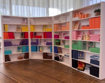 May include: A miniature white bookshelf unit filled with colorful books, decorative items, and a small potted plant. The unit is arranged in a zig-zag pattern, with the number "25" visible on one section.