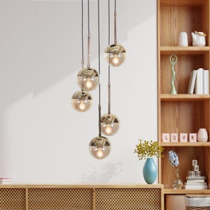 May include: A set of five gold globe pendant lights with clear glass shades hanging from a white ceiling. The lights are suspended at different heights, creating a staggered effect.