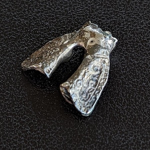 Peut inclure: Un pendentif argenté en forme de U avec des motifs en relief complexes. Le pendentif a une apparence vieillie, suggérant un style antique ou vintage. Les détails comprennent des motifs ornés et une surface texturée, lui donnant un aspect unique et artisanal.