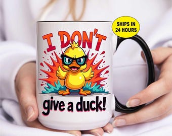 May include: White ceramic mug with a black handle and rim. The mug features a cartoon duck wearing glasses with the text "I DON'T give a duck!" in red and black. The duck is yellow with blue accents.