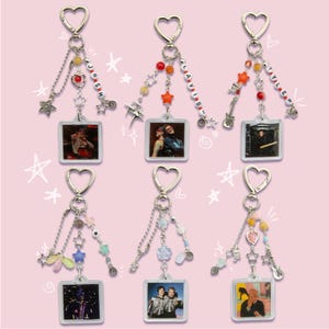 Peut inclure: Six porte-clés avec des fermoirs en forme de cœur et des breloques pendantes. Chaque porte-clés présente une petite image carrée et des perles décoratives. Certains porte-clés ont des breloques en forme d'étoile et de guitare, et certains ont des noms épelés en perles.