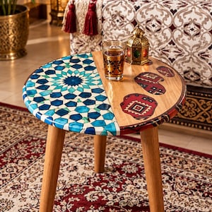 Peut inclure: Une table d'appoint ronde en bois avec trois pieds fuselés. Une moitié du plateau présente un motif géométrique en mosaïque bleu et blanc, tandis que l'autre moitié affiche un grain de bois naturel avec trois pièces de tissu incrustées.