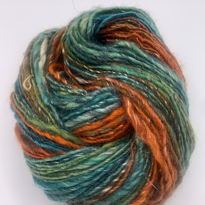 Puede incluir: Una madeja de hilo colorido con una mezcla de tonos turquesa, naranja, verde y crema. El hilo parece grueso y texturizado, adecuado para proyectos de tejido o ganchillo. Los colores están mezclados por toda la madeja.