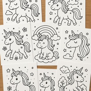Op de afbeelding: Een verzameling van acht witte kaarten met zwarte lijntekeningen van eenhoorns. Elke kaart toont een andere eenhoornsc&egrave;ne, inclusief regenbogen, sterren, wolken en bloemen. De illustraties zijn eenvoudig en geschikt om in te kleuren.