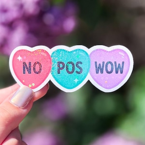 May include: Three heart-shaped stickers with glitter. The first sticker is pink and says 'NO', the second sticker is teal and says 'POS', and the third sticker is purple and says 'WOW'.