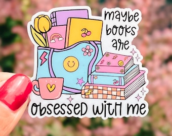 May include: A colorful sticker featuring a whimsical illustration of books, a coffee cup, and a flower. The sticker has the text "maybe books are obsessed with me". The design includes a rainbow, a smiley face, and stars.