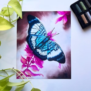 Könnte beinhalten: Ein blauer und weißer Schmetterling mit schwarzen Markierungen sitzt auf einer rosa Blume. Die Flügel des Schmetterlings sind weit ausgebreitet, und die Blume blüht in voller Pracht. Der Hintergrund ist in einem sanften Braunton gehalten.