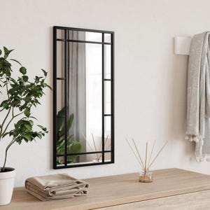 Peut inclure: Un miroir rectangulaire à cadre noir avec un motif de grille est monté sur un mur blanc. Le miroir reflète un aperçu de verdure et une fenêtre. Une commode en bois contient une plante en pot, du tissu plié et un diffuseur de roseaux.