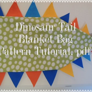 May include: A green fabric with white polka dots, shaped like a dinosaur tail, with a blue, orange, and yellow triangle pattern along the edge. The fabric has the text "Dinosaur Tail Blanket Bag Pattern Tutorial, pdf." printed on it.