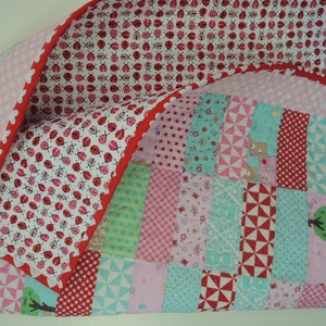May include: A patchwork quilt with a red, white, and blue color scheme. The quilt is made of various fabrics with different patterns, including polka dots, stripes, and floral designs. The quilt is folded in half and has a scalloped edge.