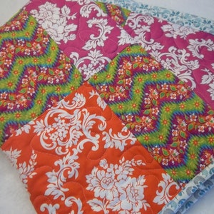 May include: A patchwork quilt with a variety of colorful patterns, including pink, orange, green, and white. The quilt is made of different fabrics with floral and geometric designs.
