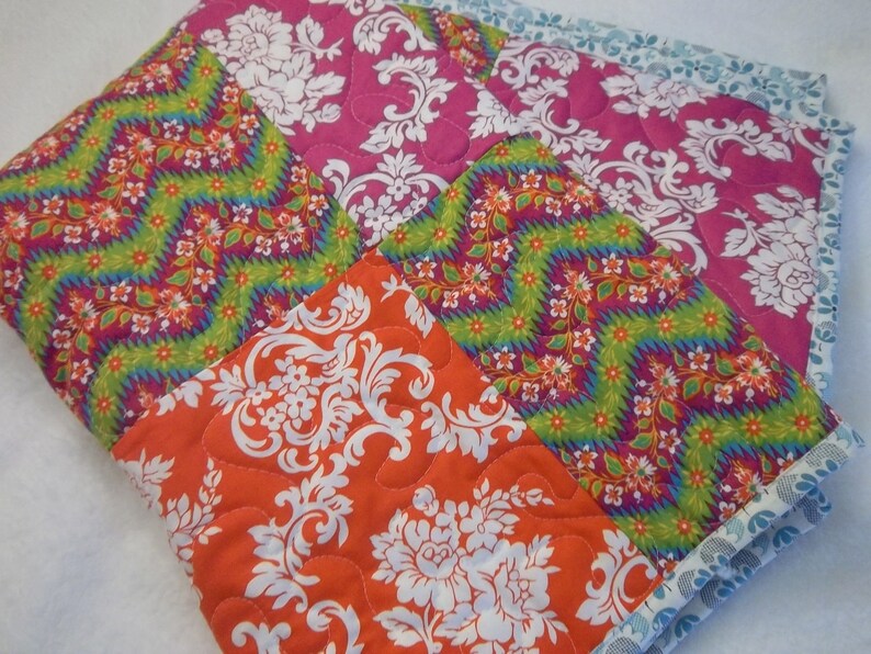 May include: A patchwork quilt with a variety of colorful patterns, including pink, orange, green, and white. The quilt is made of different fabrics with floral and geometric designs.