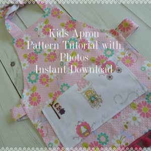 May include: Pink and white kids apron with a floral print and a white pocket. The apron has a tie at the neck and two straps that tie at the waist. The text "Kids Apron Pattern Tutorial with Photos Instant Download" is printed on the apron.