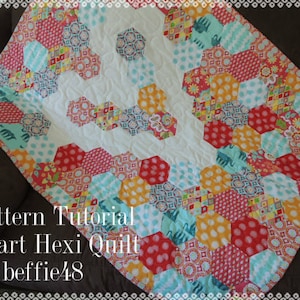 May include: A heart-shaped quilt made with colourful hexagonal fabric patches. The quilt is made in a variety of colours, including red, orange, yellow, blue, and green. The quilt is quilted with a white thread. The quilt is titled "Heart Hexi Quilt by beffie48".
