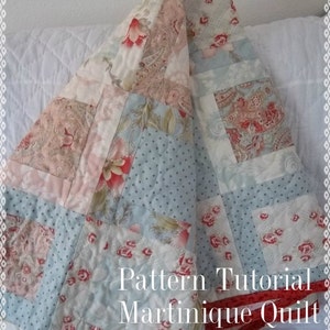 May include: A patchwork quilt with a blue, white and pink floral pattern. The quilt is folded in a triangular shape and has the text "Pattern Tutorial Martinique Quilt by beffie48" on the bottom.