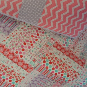 May include: A patchwork quilt with a variety of pink, red, white, and purple fabrics. The quilt is made up of different patterns, including polka dots, stripes, and flowers.