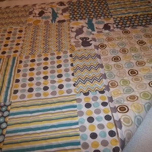May include: A patchwork baby quilt with a variety of patterns in shades of gray, yellow, and blue. The quilt features a polka dot pattern, stripes, zigzags, and a button pattern.