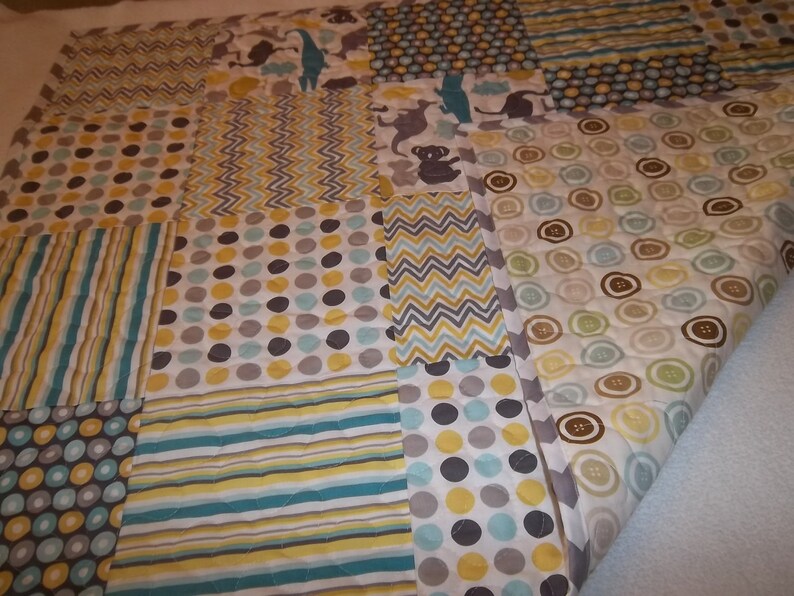 May include: A patchwork baby quilt with a variety of patterns in shades of gray, yellow, and blue. The quilt features a polka dot pattern, stripes, zigzags, and a button pattern.