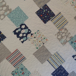 May include: A white baby quilt with a diamond pattern. The quilt is made of various fabrics with different patterns, including clouds, stars, rockets, and stripes. The quilt is quilted with a wavy pattern.