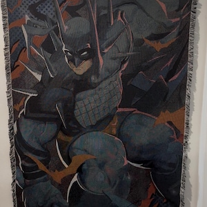 Puede incluir: Manta tejida con una ilustración de Batman en tonos azules, grises y naranjas. El diseño muestra a Batman en una pose dinámica, con su capucha y el símbolo del murciélago. La manta tiene un borde con flecos y es adecuada para un sofá o cama.