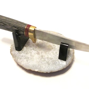 May include: A hunting knife with a wooden handle and a silver blade is displayed on a white agate stand. The handle has a red and gold accent.