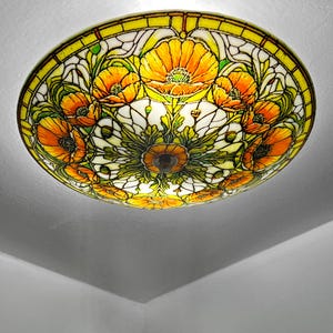 May include: A stained glass ceiling light fixture featuring a floral design with orange and yellow poppies. The light has a circular shape with a yellow border and a central brown fixture.