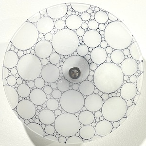 May include: A white glass ceiling light fixture with a circular design. The fixture has a silver metal center and is covered in a pattern of small, black circles.