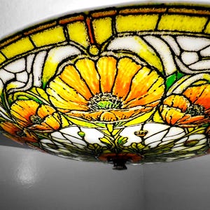 May include: A stained glass ceiling light fixture featuring a floral design with orange and yellow flowers, green leaves, and white accents. The fixture has a black metal base and is mounted on a white ceiling.