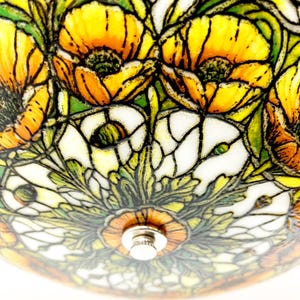 May include: Close-up of a stained glass lamp shade featuring a floral design. The shade has a pattern of yellow and orange poppies, white flowers, and green leaves. The lamp has a metal fixture in the center.
