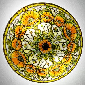 May include: A round, stained glass lamp shade featuring a floral design. The shade has a yellow border and a central pattern of orange poppies with green leaves and white background. The lamp shade is a decorative lighting fixture.