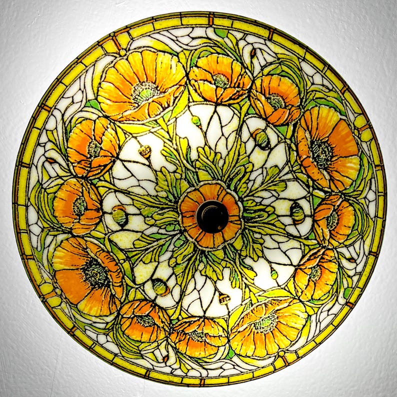May include: A round, stained glass lamp shade featuring a floral design. The shade has a yellow border and a central pattern of orange poppies with green leaves and white background. The lamp shade is a decorative lighting fixture.