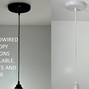 May include: Two pendant light fixtures with hardwired canopy options. One has a black canopy and cord, the other has a white canopy and cord. The text in the image reads: HARDWIRED CANOPY OPTIONS AVAILABLE, WHITE AND BLACK.