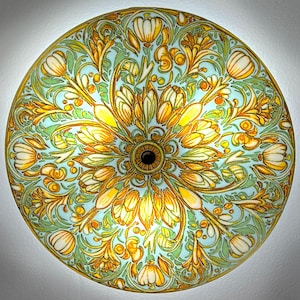 May include: A round, decorative ceiling light fixture with a floral design. The light fixture features a light blue background with yellow, white, and green floral patterns. The center has a dark brown circle.