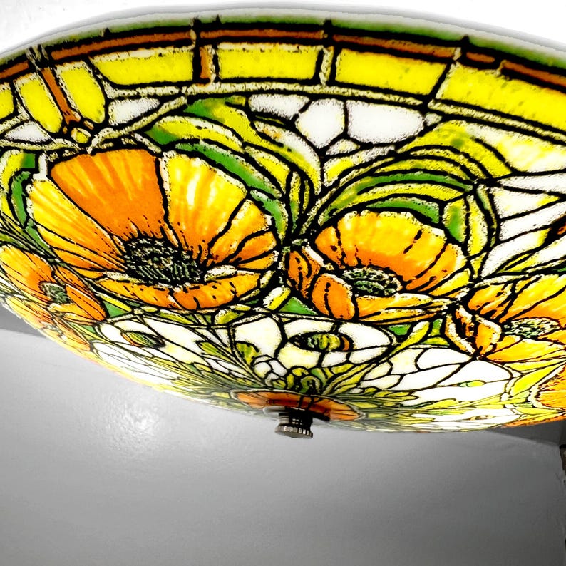 May include: A stained glass ceiling light fixture featuring a floral design with orange and yellow poppies. The flowers are set against a white and green background, with black outlines. The fixture has a metal base.